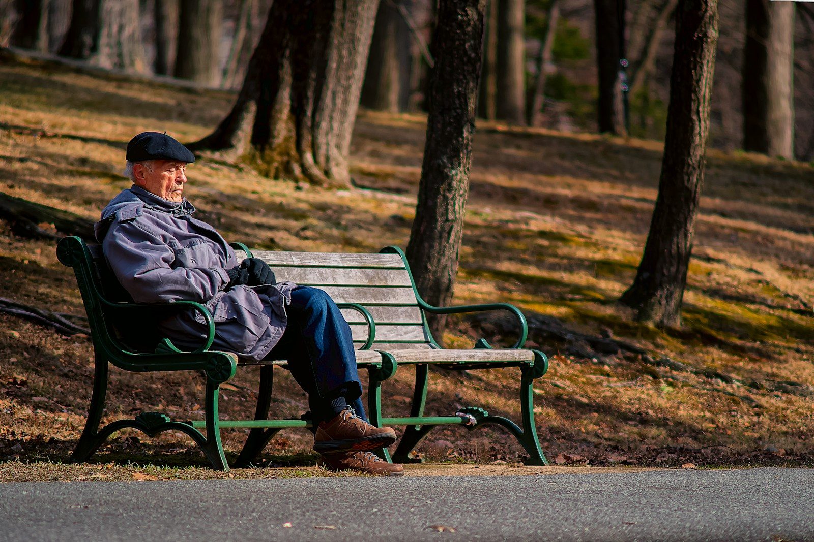 man in black jacket sitting on brown wooden bench